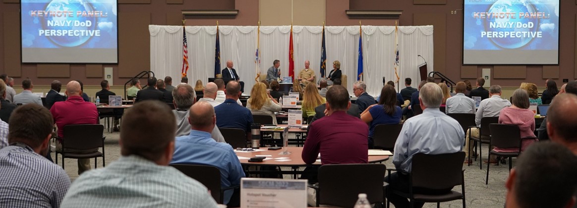 A group of people sit in a conference. 